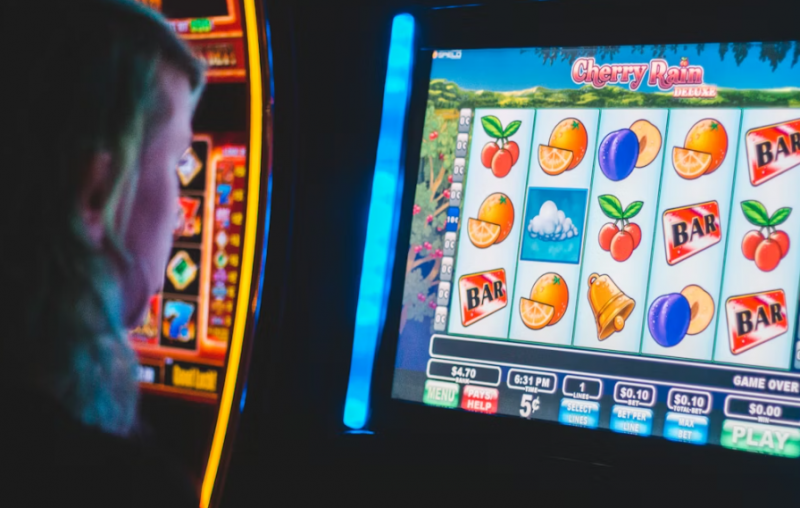 Photo of a person playing a Cherry Rain Deluxe slot machine with fruit symbols on the screen